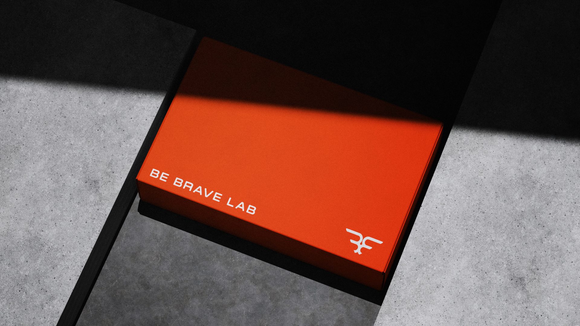 Caixa laranja da Be Brave Lab com a assinatura e o símbolo em branco, sob sombra dura