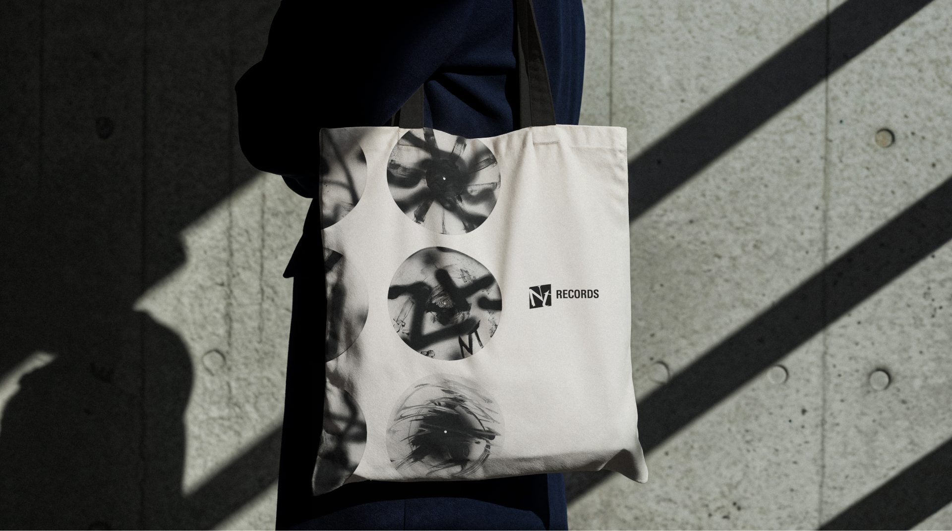Ecobag com três discos pintados em spray e o logo NT Records, no ombro diante de uma parede de concreto